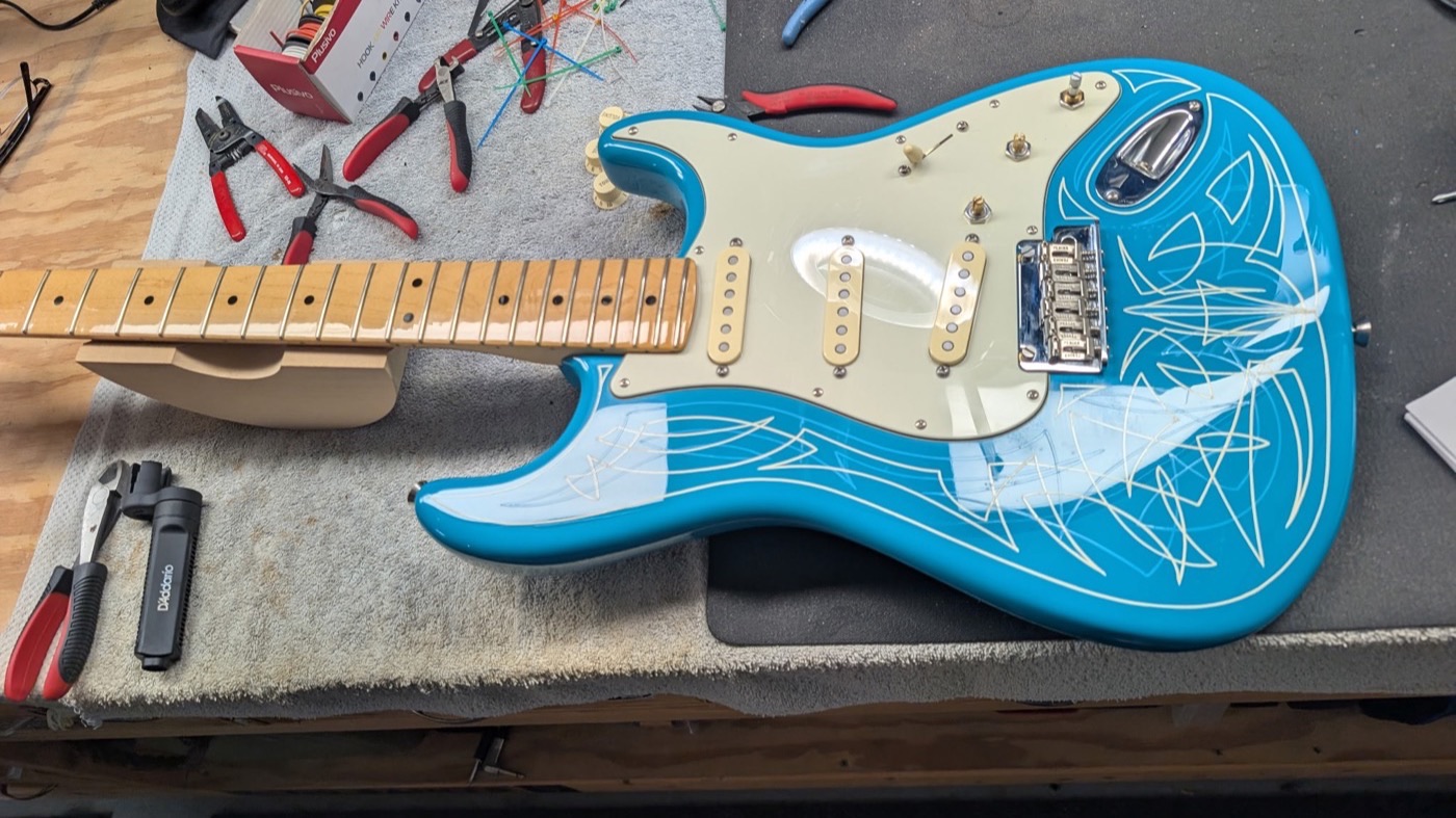 Stratocaster body reassembled with pickguard, pickups, and bridge fitted, neck alongside on the bench